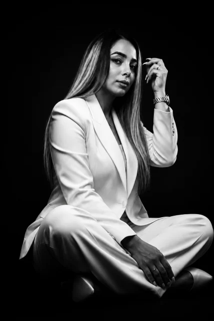 In stark monochrome, a sharply tailored ivory blazer contrasts with deep shadows, enveloping a woman of poised strength