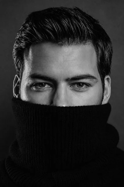 Create a hyper-realistic black and white fashion portrait based on the uploaded reference image. Keep the exact same composition, vertical framing, close portrait crop, camera angle, subject distance, background wall tex…